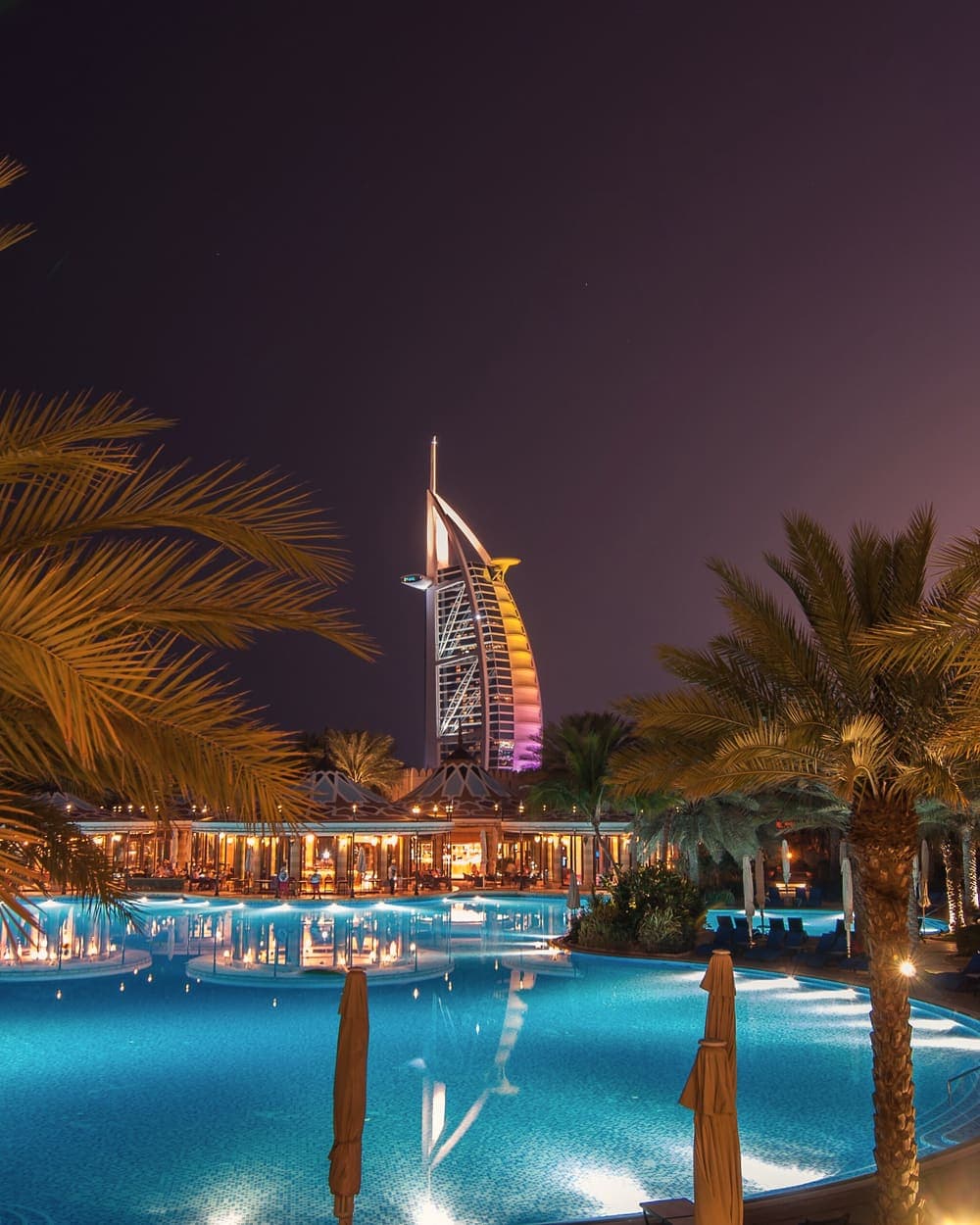 Burj Al Arab lit up at night beyond a palm-lined resort pool