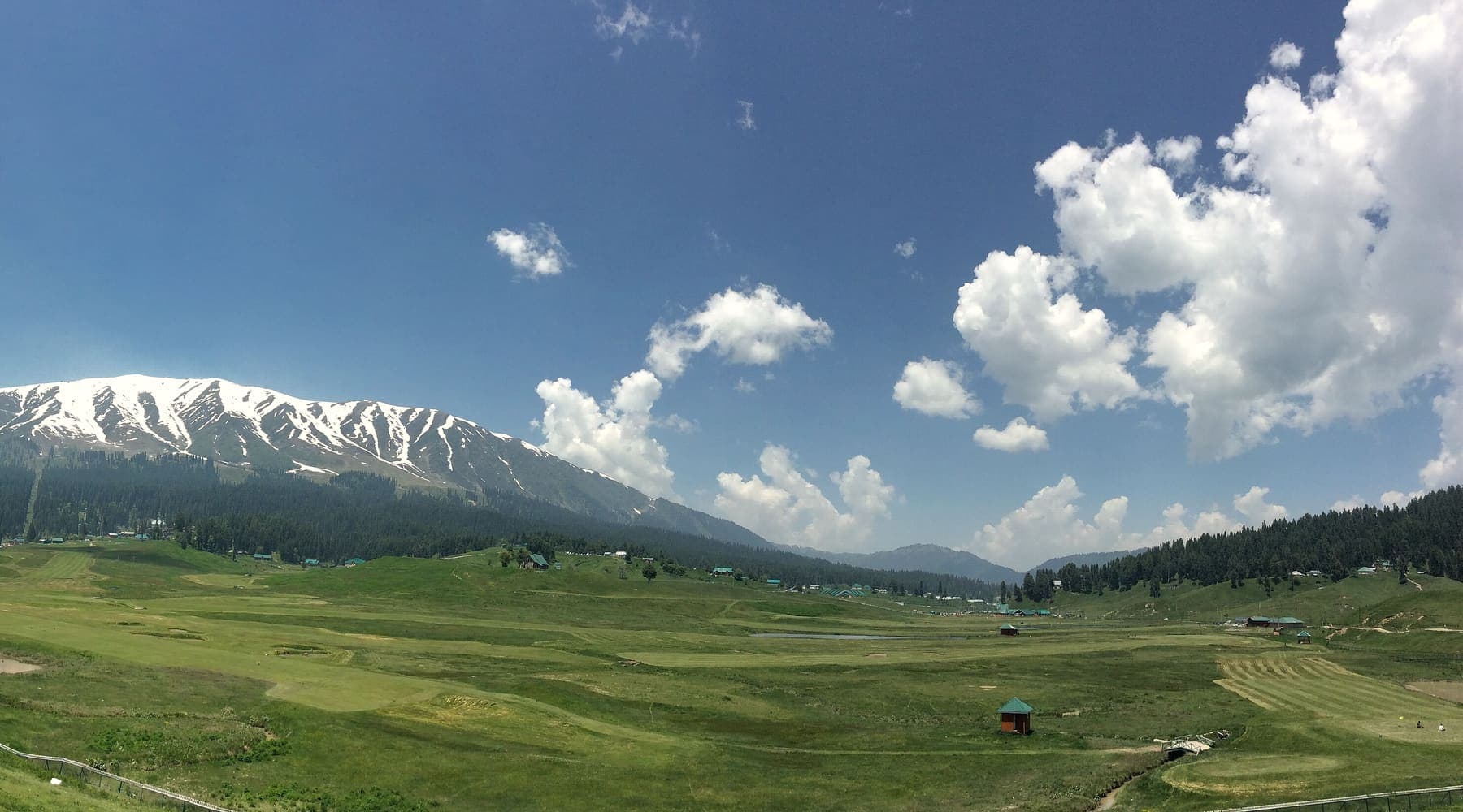 A wide green meadow below snow-capped peaks in Kashmir