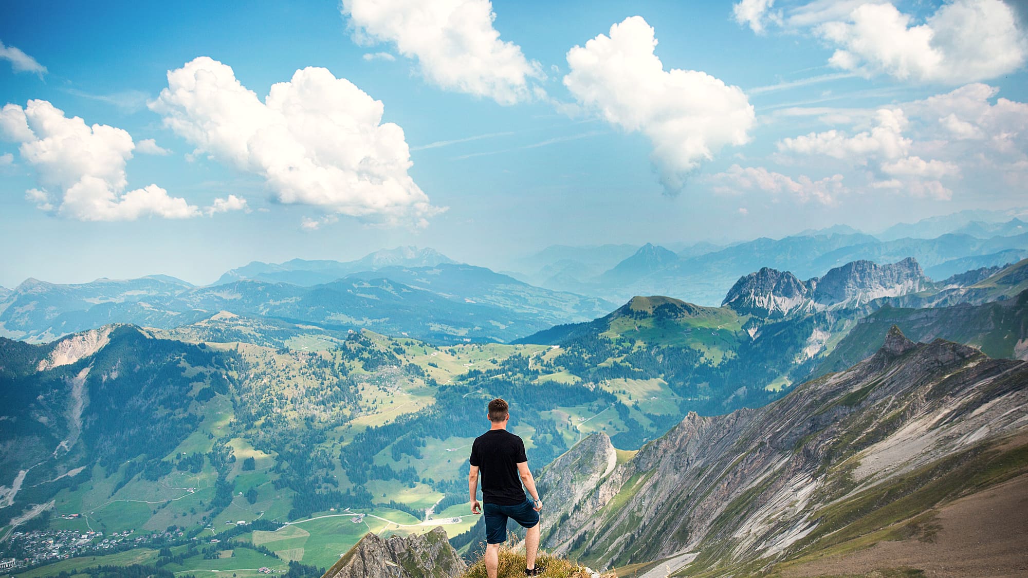 A traveller standing on a ridge above green mountain valleys
