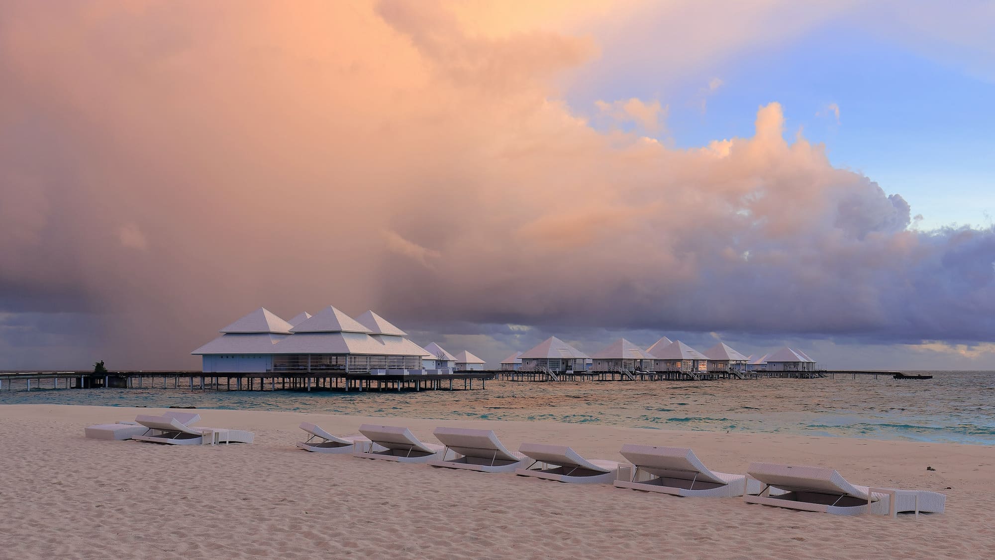 Water villas beyond a beach in the Maldives at sunset